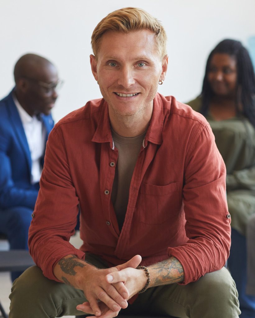 smiling-man-at-group-therapy-session-7HU8Q2C-pf2n5igpmfm4ppl9w5nt89pd7hae8a7fb8ryn904qo